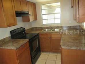A kitchen features wooden cabinets, a black stove, and a double sink with tiled floors — 4851 BILLY DIRECT LANE, LUTZ, FL