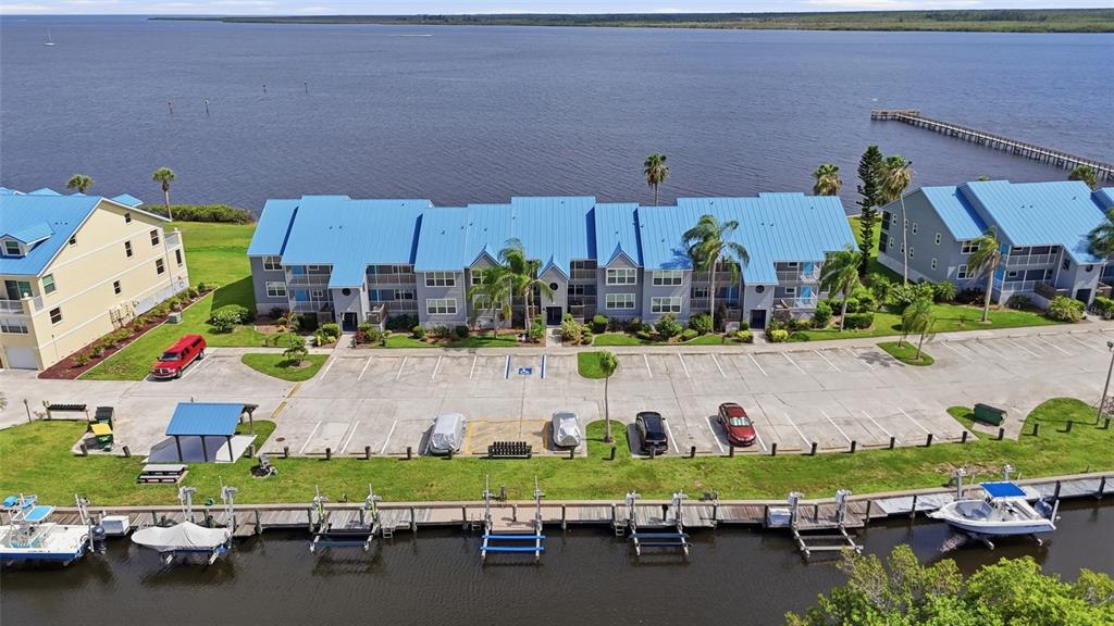 An aerial view shows a multi-story apartment building with a blue roof, parking lot, and boat docks — 4410 WARREN AVENUE UNIT 412, PORT CHARLOTTE, FL