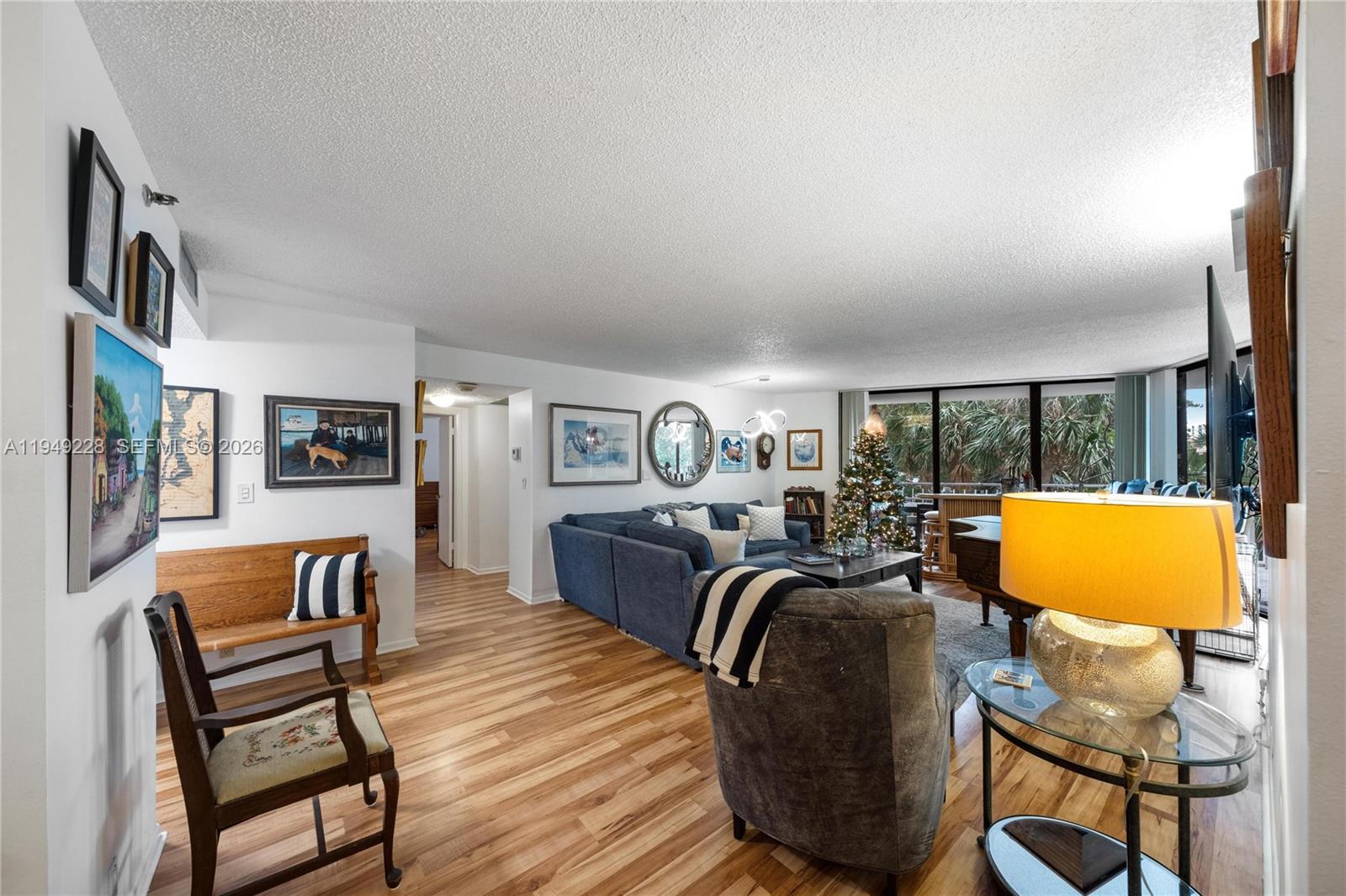 A living room features wood-look flooring, a blue sectional sofa, and a large window view — 4000 Towerside Ter # 301, Miami FL 33138, MIAMI, FL