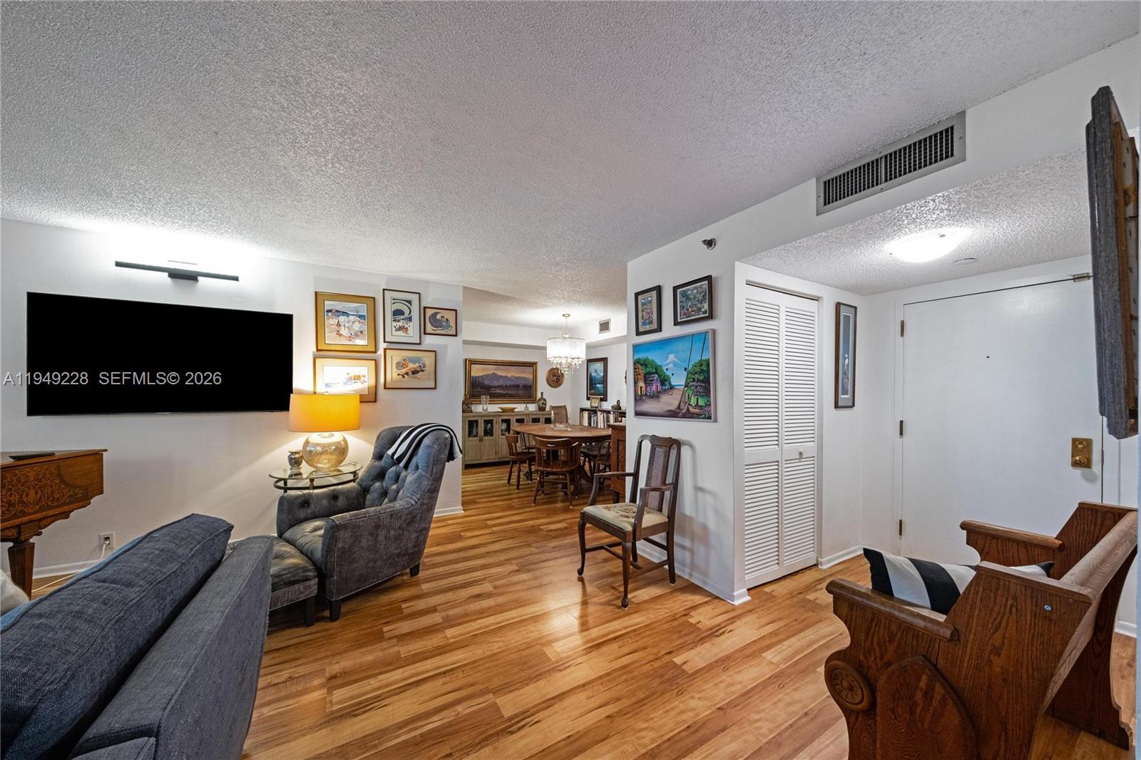 A living room with wood flooring, a television, and a dining area in the background — 4000 Towerside Ter # 301, Miami FL 33138, MIAMI, FL