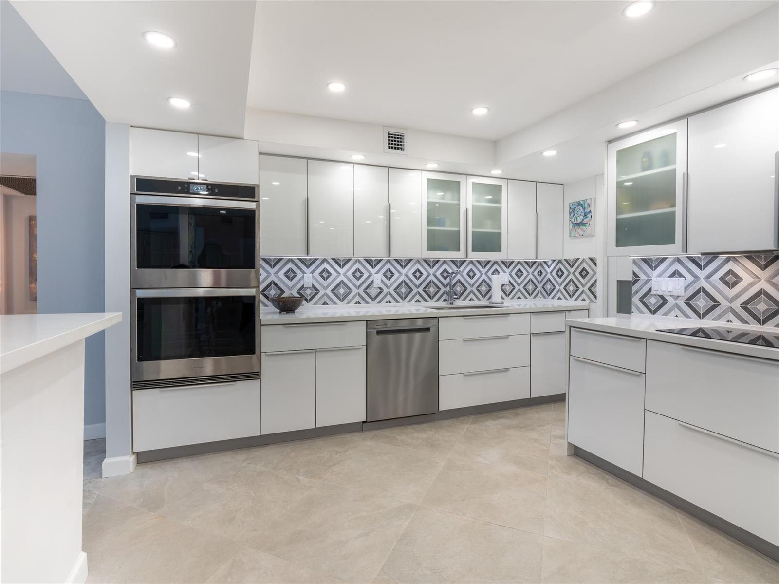 A modern kitchen features white glossy cabinets, stainless steel appliances, and a geometric patterned backsplash — 2850 N Palm Aire Drive # 601, Pompano Beach FL 33069, POMPANO BEACH, FL