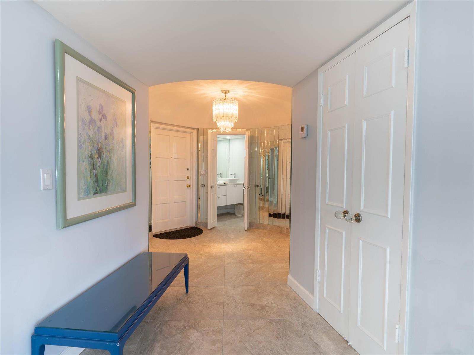 A hallway features light-colored tile flooring, a crystal chandelier, mirrored walls, and a blue bench — 2850 N Palm Aire Drive # 601, Pompano Beach FL 33069, POMPANO BEACH, FL