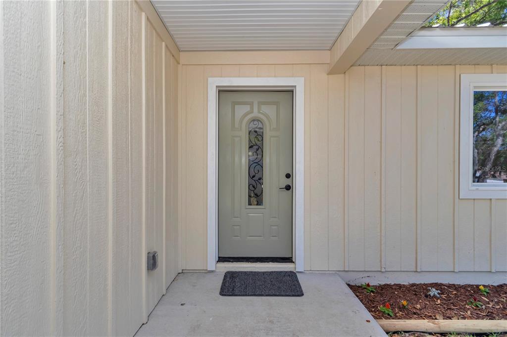 A light green front door with a decorative glass insert sits under a covered entryway — 2778 W CYPRESS DRIVE, DUNNELLON, FL