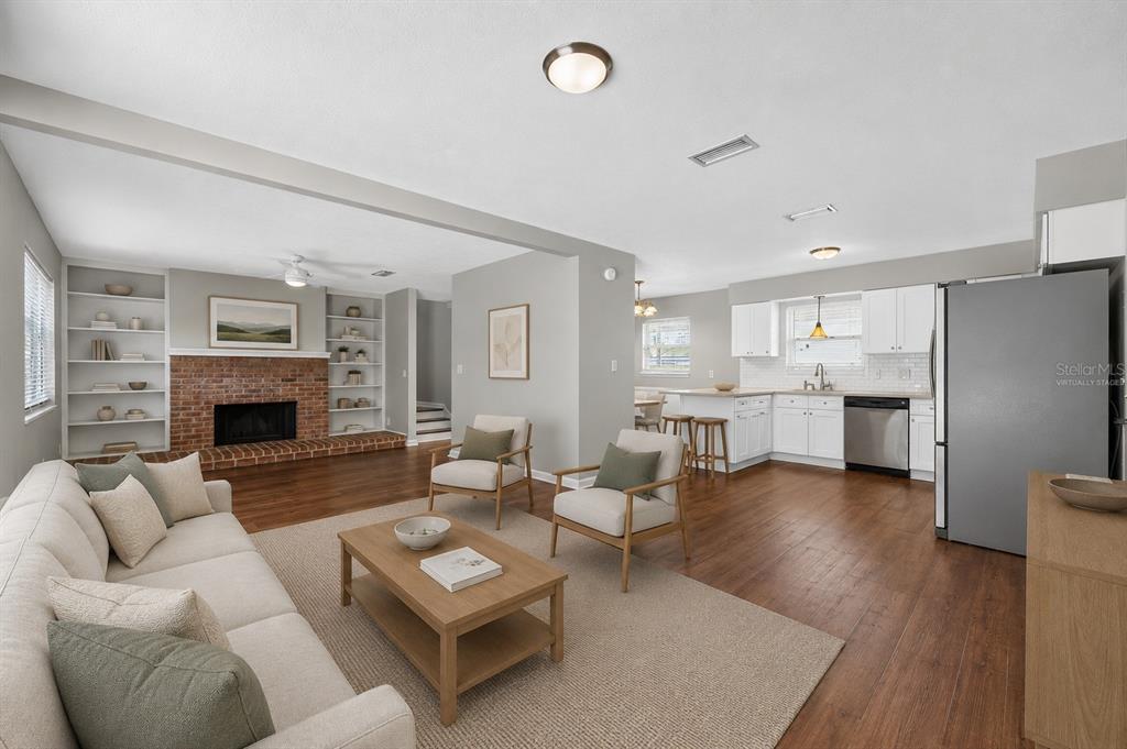 An open-concept living room and kitchen featuring a brick fireplace, wood flooring, and white cabinetry — 1543 REDBUD COURT, ORANGE PARK, FL