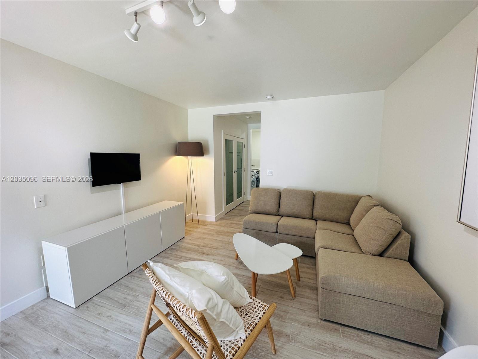 A living room features a beige sectional sofa, white media console, and a rattan chair — 745 13th St # 6, Miami Beach FL 33139, MIAMI BEACH, FL
