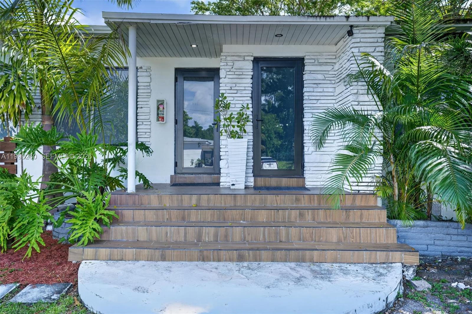 A house exterior features a tiled staircase leading to two glass doors and white stone walls — 7811 NE 10th Ct, Miami FL 33138, MIAMI, FL
