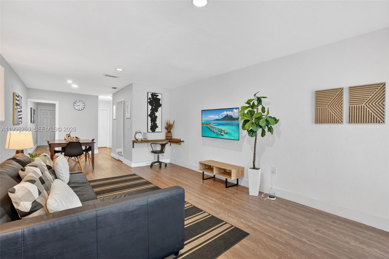 A living room features a dark sofa, a wall-mounted television, and a small desk area — 7811 NE 10th Ct, Miami FL 33138, MIAMI, FL