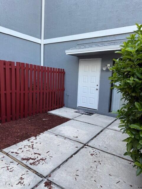 A white door opens onto a concrete patio next to a red wooden fence — 1 Crossings Circle W # C, Boynton Beach FL 33435, BOYNTON BEACH, FL