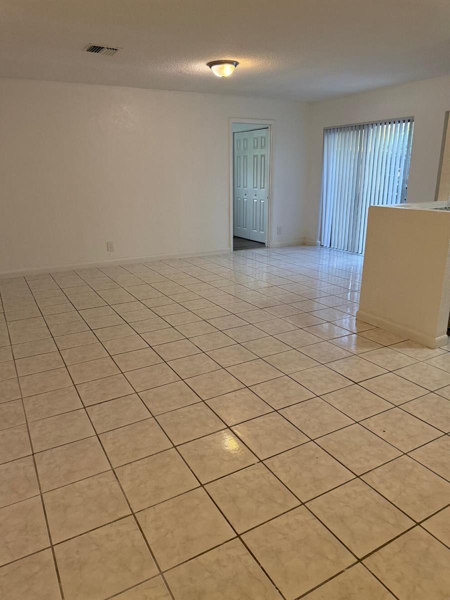 An empty room with light-colored tile flooring, white walls, and a sliding glass door — 1 Crossings Circle W # C, Boynton Beach FL 33435, BOYNTON BEACH, FL