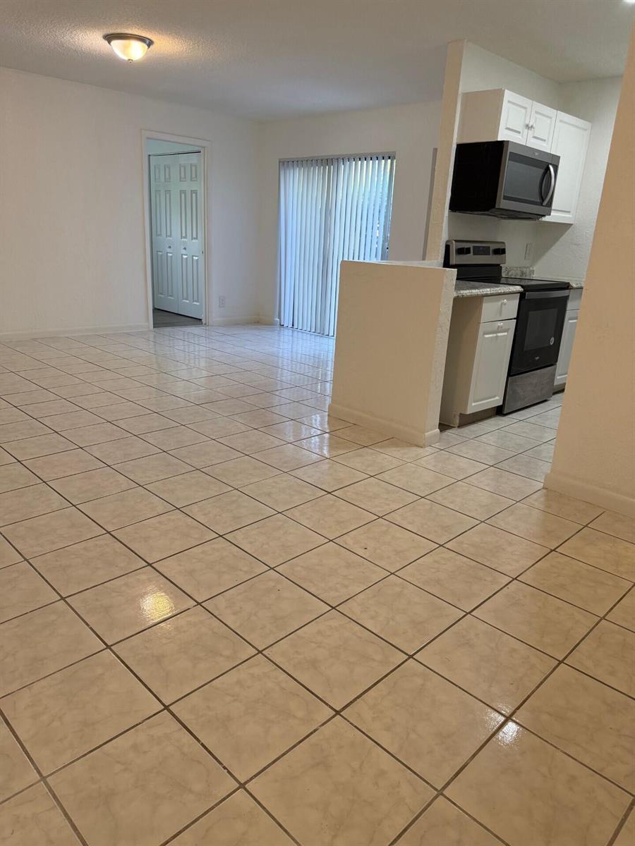 An open-concept kitchen and living area features light-colored tile flooring and white cabinetry — 1 Crossings Circle W # C, Boynton Beach FL 33435, BOYNTON BEACH, FL