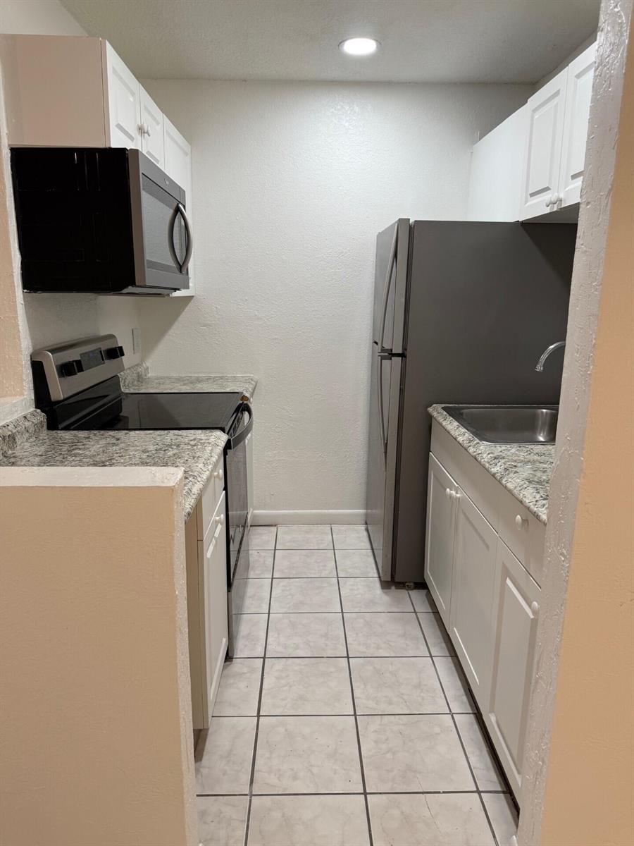 A galley kitchen features white cabinets, granite-look countertops, stainless steel appliances, and tiled flooring — 1 Crossings Circle W # C, Boynton Beach FL 33435, BOYNTON BEACH, FL