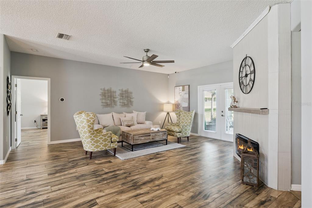 A living room features wood-look flooring, a fireplace, a ceiling fan, and patterned armchairs — 515 JUNE AVENUE, HAINES CITY, FL