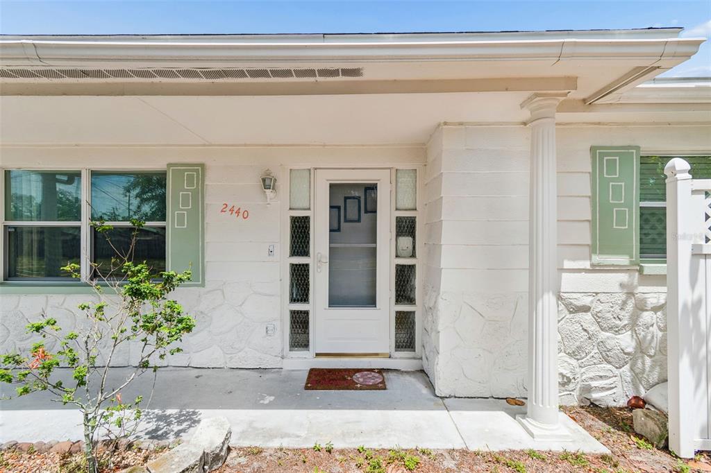 A white house exterior features a front porch, a storm door, and decorative green shutters — 2440 ARCADIA ROAD, HOLIDAY, FL