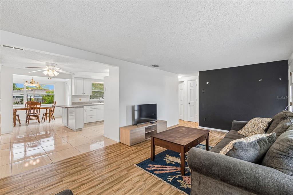 A living room with wood-look flooring and a black accent wall opens to a kitchen — 2440 ARCADIA ROAD, HOLIDAY, FL