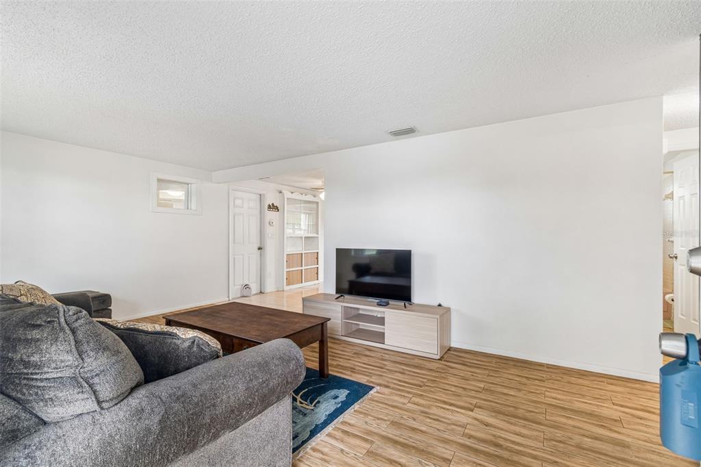 A living room features wood-look tile flooring, white walls, a television console, and a sofa — 2440 ARCADIA ROAD, HOLIDAY, FL