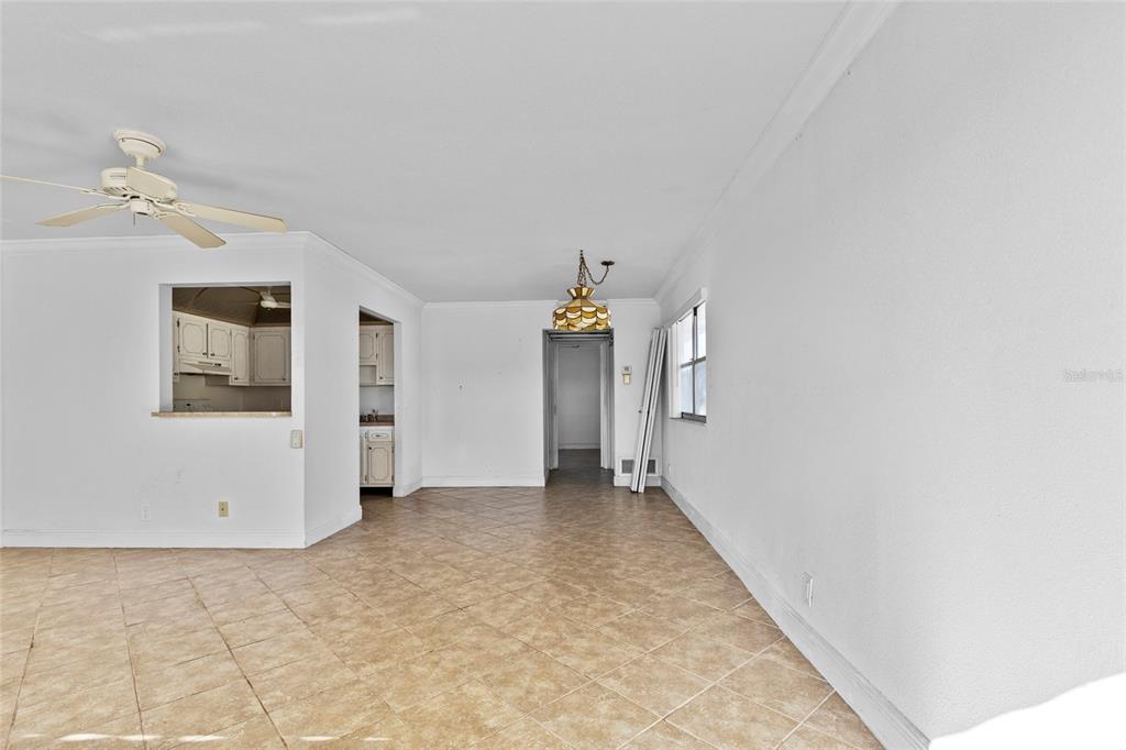 An empty room with beige tile flooring, a ceiling fan, and a pass-through kitchen window — 187 SAXONY TERRACE UNIT D, DELRAY BEACH, FL