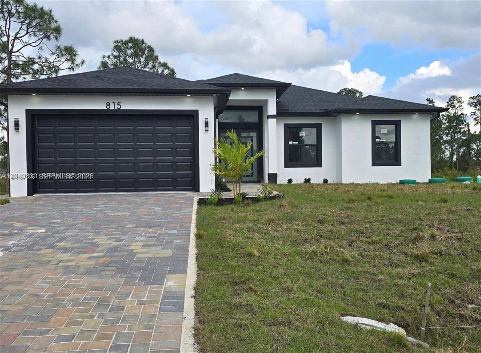 A single-story house with white stucco walls, a black roof, and a paved driveway — 815 Anaconda Ave S, Lehigh Acres FL 33974, LEHIGH ACRES, FL