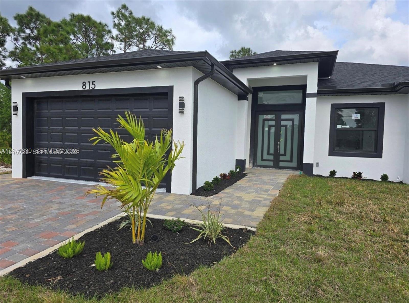 A modern single-story house exterior features a white stucco facade, black trim, and double doors — 815 Anaconda Ave S, Lehigh Acres FL 33974, LEHIGH ACRES, FL