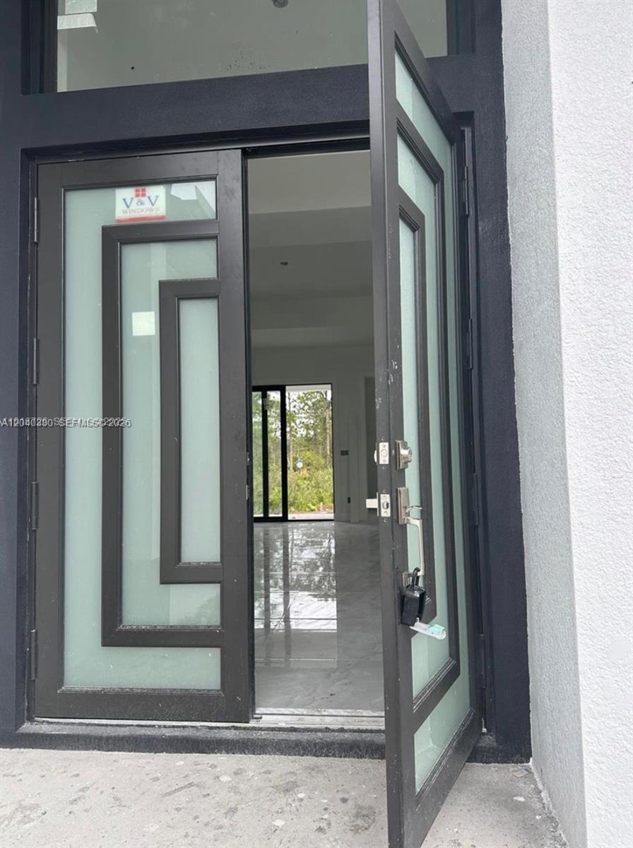 A modern front door with frosted glass panels stands open to a bright, tiled interior — 815 Anaconda Ave S, Lehigh Acres FL 33974, LEHIGH ACRES, FL