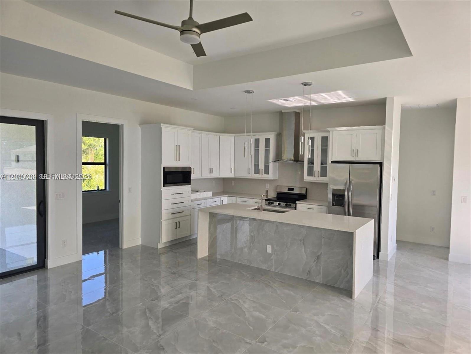 A modern kitchen features white cabinetry, a gray marble-patterned island, and polished tile flooring — 815 Anaconda Ave S, Lehigh Acres FL 33974, LEHIGH ACRES, FL