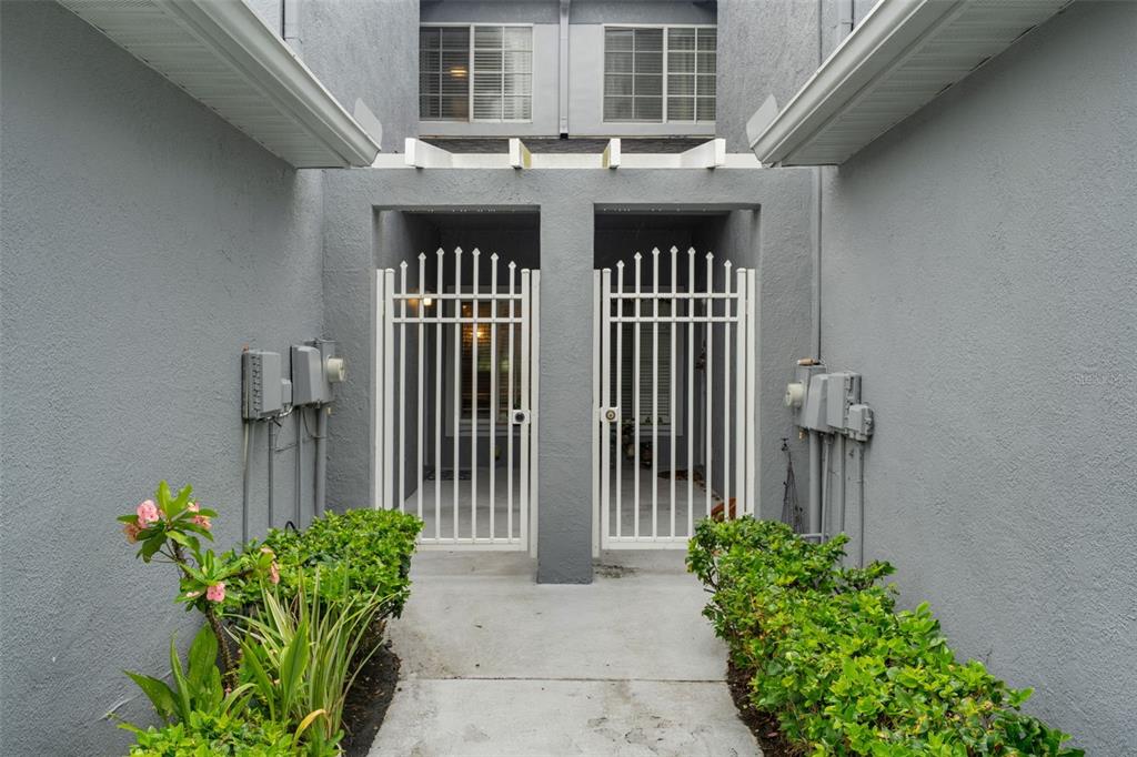 A concrete walkway leads to two white metal gates between gray stucco walls — 18105 NASSAU POINT DRIVE, TAMPA, FL