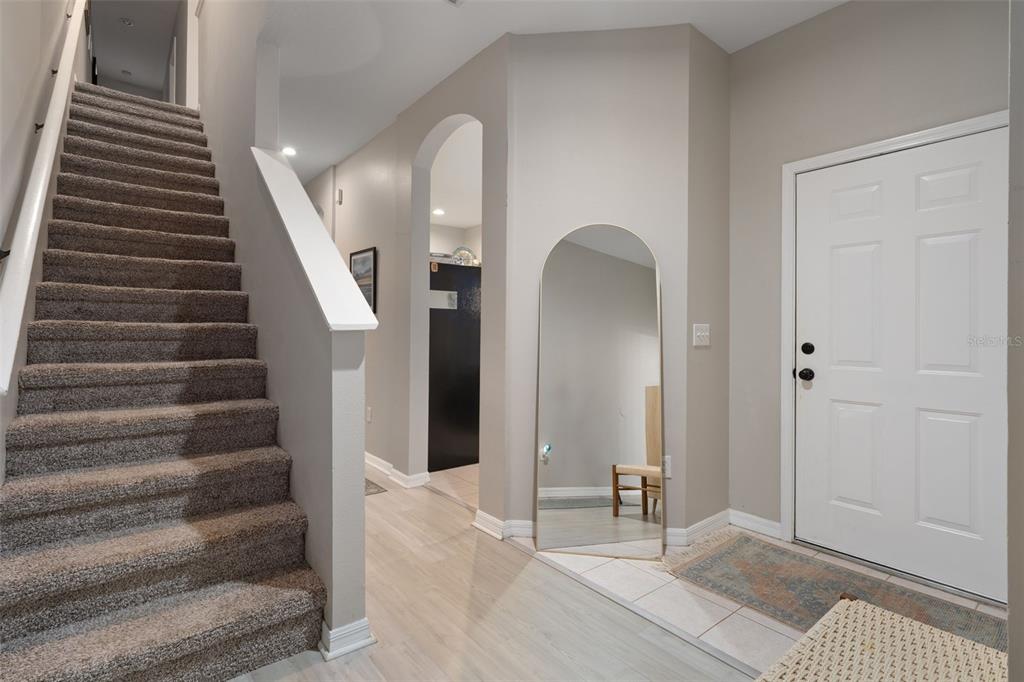 An entryway features a carpeted staircase, light wood flooring, an arched mirror, and a door — 18105 NASSAU POINT DRIVE, TAMPA, FL