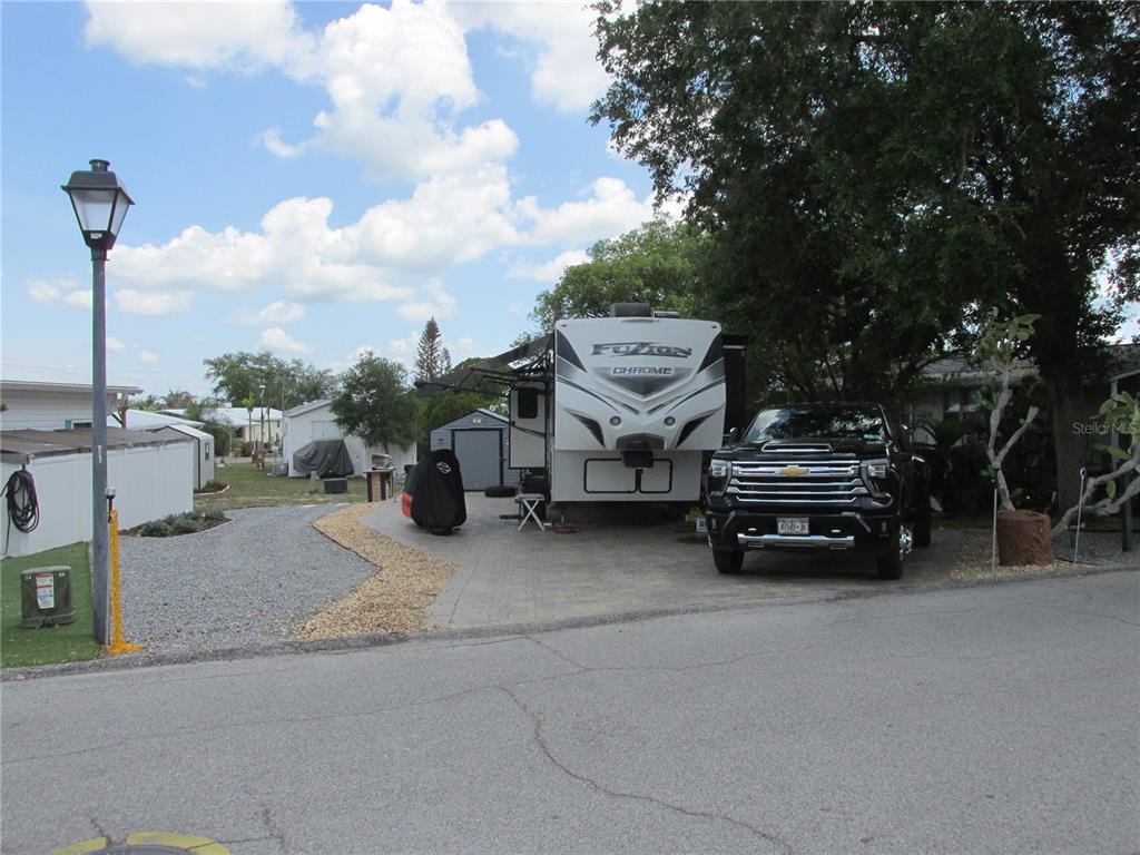 A black pickup truck is parked next to a large RV on a paved driveway — 16 SADDLEBAG TRAIL S, LAKE WALES, FL