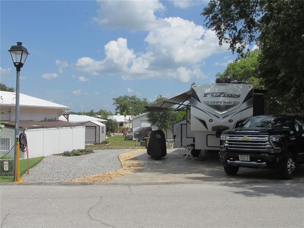 A black pickup truck is parked next to a large RV on a paved driveway — 16 SADDLEBAG TRAIL S, LAKE WALES, FL