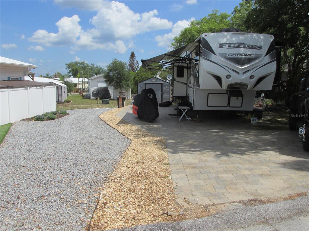 A large recreational vehicle is parked on a paved driveway next to a gravel area — 16 SADDLEBAG TRAIL S, LAKE WALES, FL