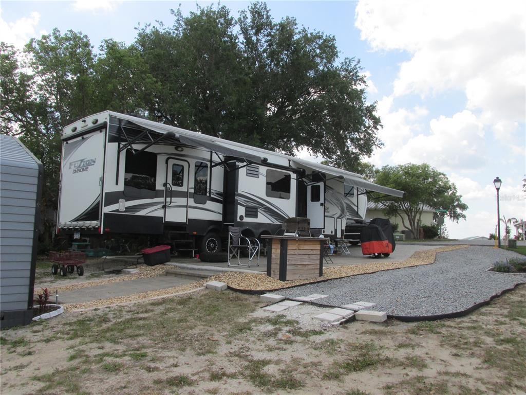 A large recreational vehicle is parked on a gravel lot next to a small shed — 16 SADDLEBAG TRAIL S, LAKE WALES, FL