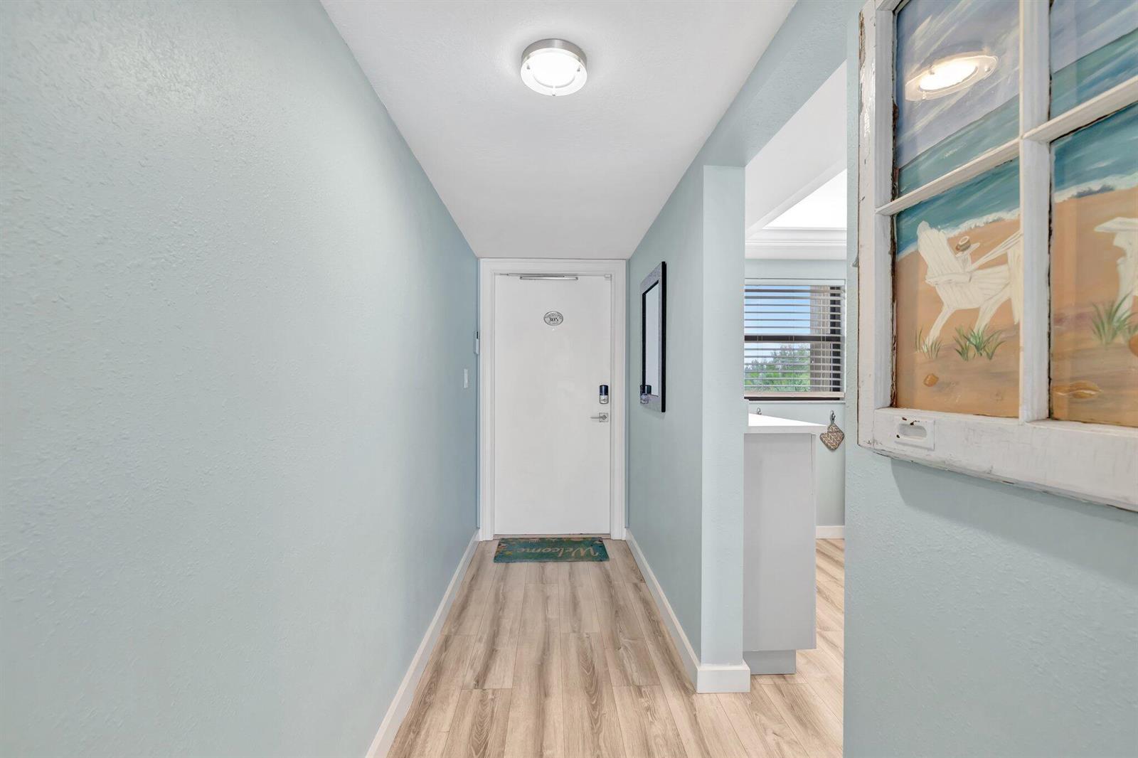 A light blue entryway features wood-look flooring, a white door, and a decorative window frame — 10310 S Ocean Drive # 305, Jensen Beach FL 34957, JENSEN BEACH, FL