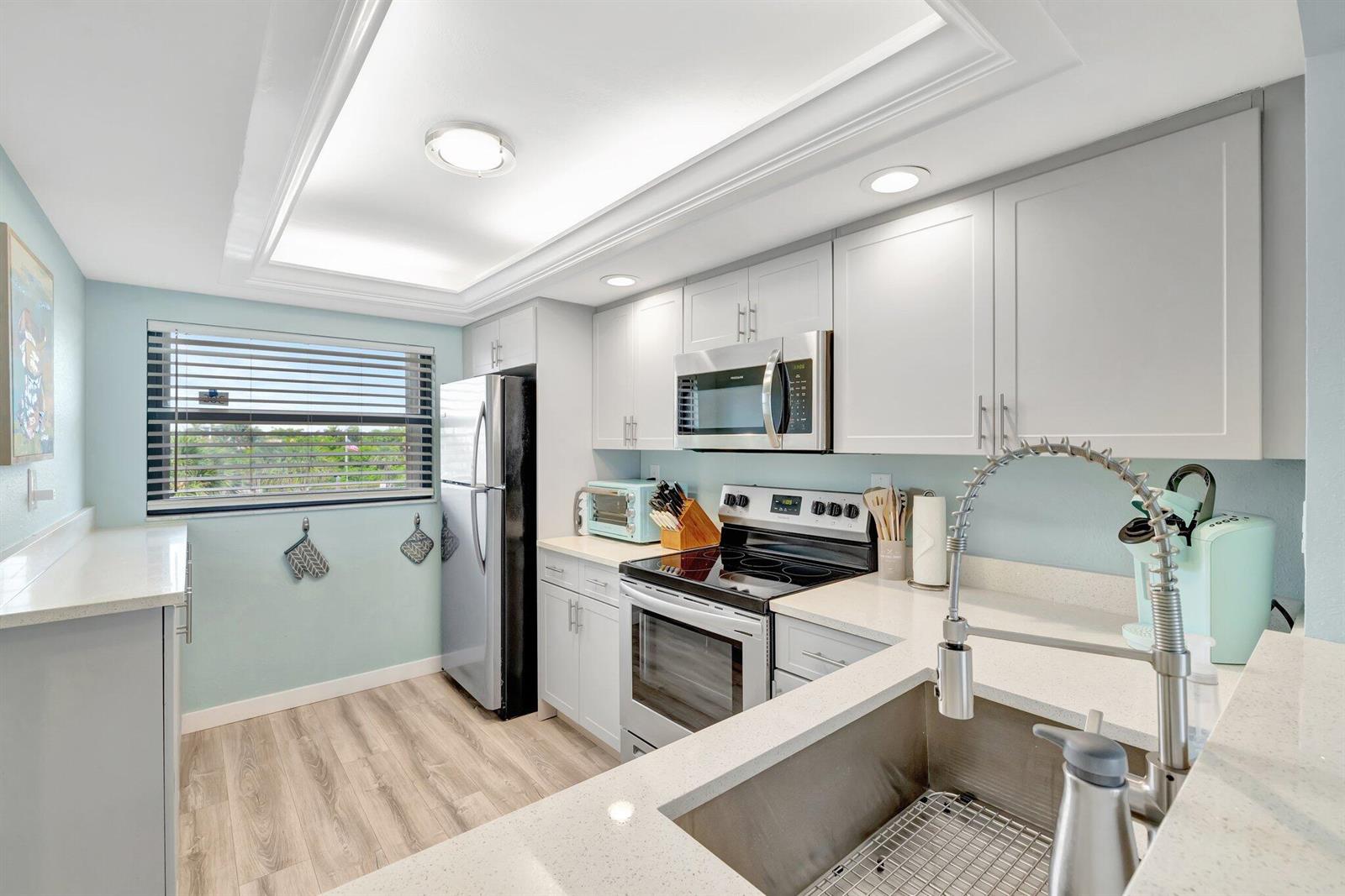 A kitchen features light blue walls, white cabinets, stainless steel appliances, and quartz countertops — 10310 S Ocean Drive # 305, Jensen Beach FL 34957, JENSEN BEACH, FL