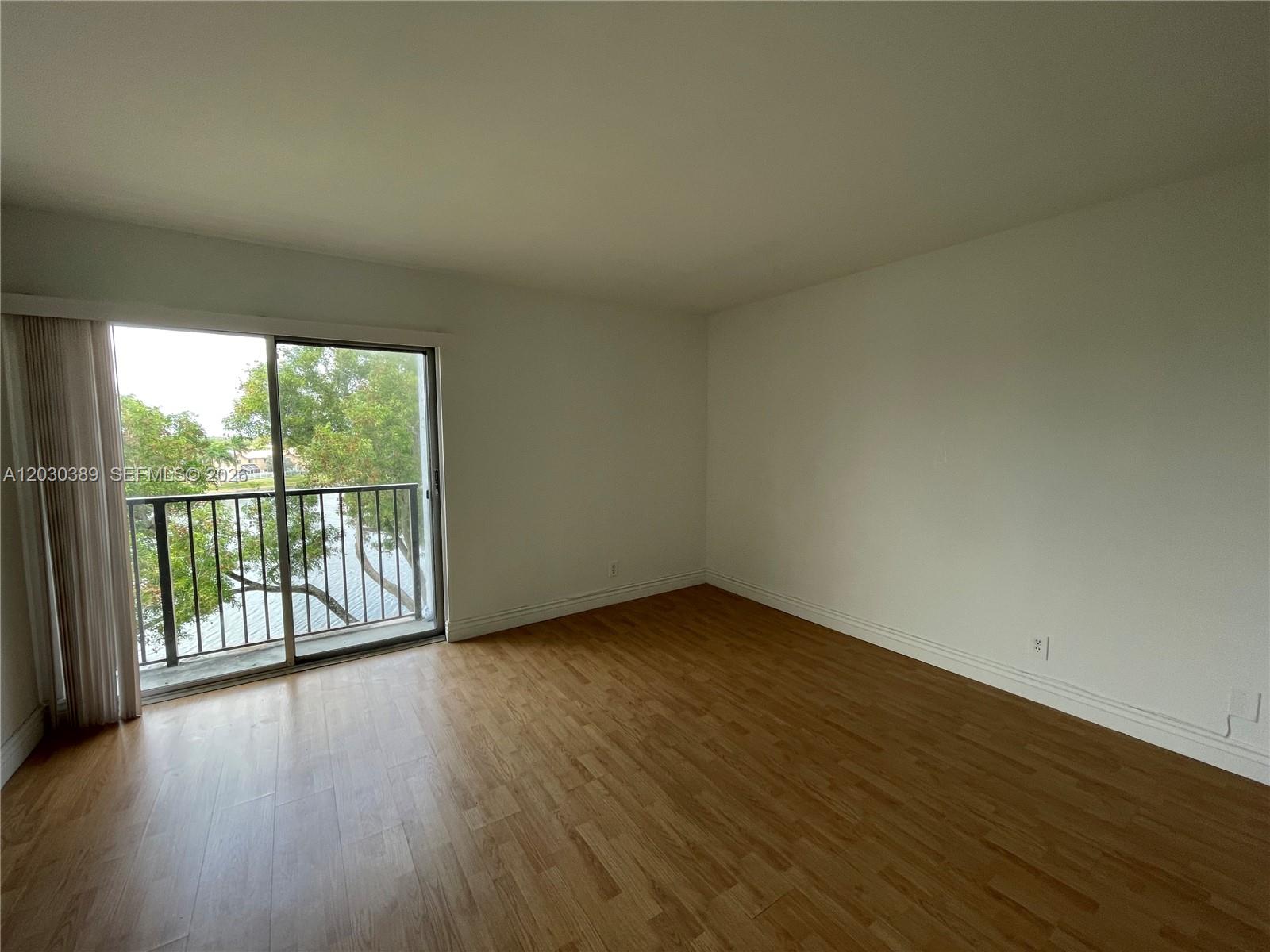 An empty room features light wood-look flooring, white walls, and a sliding glass door to a balcony — 8560 N Sherman Cir # 504, Miramar FL 33025, MIRAMAR, FL