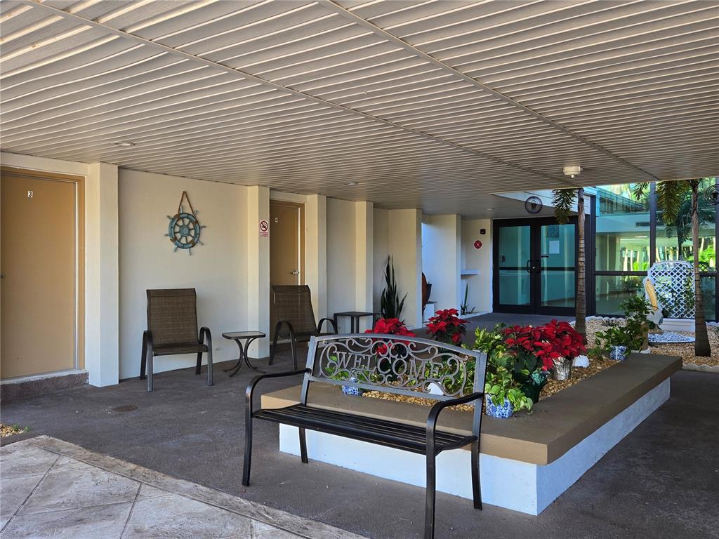 A covered outdoor patio features a welcome bench, chairs, and potted poinsettias near building entrances — 21260 BRINSON AVENUE UNIT 307, PORT CHARLOTTE, FL