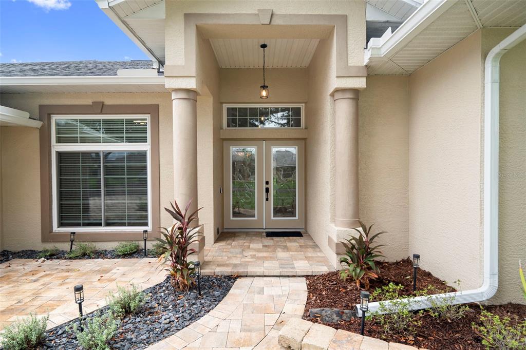 The exterior of a house features a paved walkway leading to a double-door entryway — 6245 SILVER OAKS DRIVE, ZEPHYRHILLS, FL