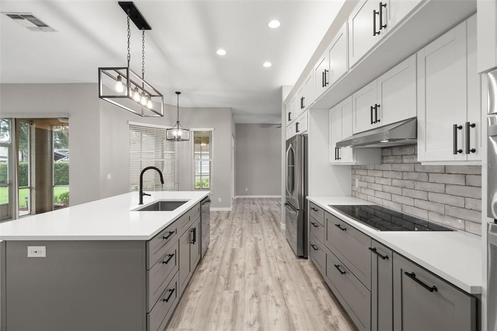 A modern kitchen features a gray island with a sink, white upper cabinets, and gray lowers — 6245 SILVER OAKS DRIVE, ZEPHYRHILLS, FL
