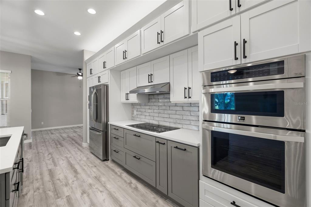 A modern kitchen features white upper cabinets, grey lower cabinets, stainless steel appliances, and tile backsplash — 6245 SILVER OAKS DRIVE, ZEPHYRHILLS, FL
