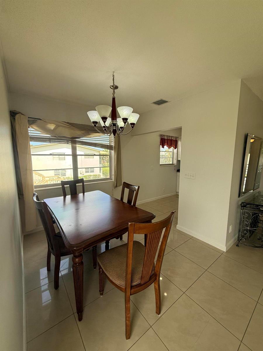 A dining room features a wooden table, four chairs, a chandelier, and light-colored tile flooring — 184 Easthampton H, West Palm Beach FL 33417, WEST PALM BEACH, FL