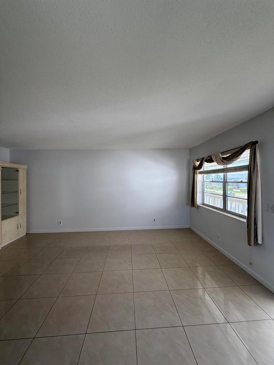 An empty room with light-colored tile flooring, a large window with curtains, and a cabinet — 184 Easthampton H, West Palm Beach FL 33417, WEST PALM BEACH, FL
