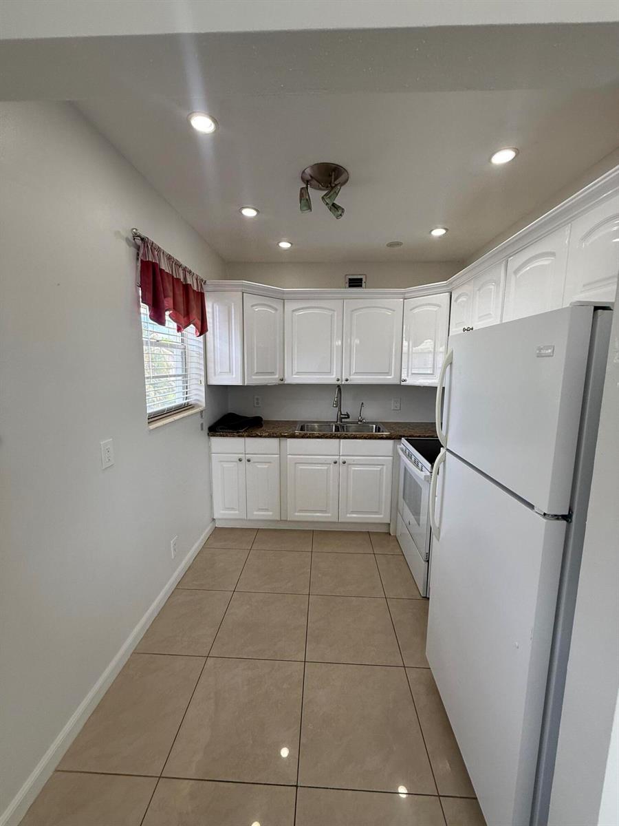 A kitchen features white cabinets, a double sink, a white refrigerator, and tiled flooring — 184 Easthampton H, West Palm Beach FL 33417, WEST PALM BEACH, FL