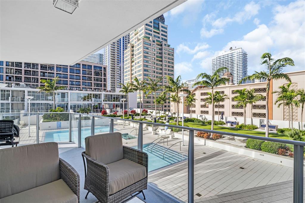 A balcony with outdoor seating overlooks a swimming pool, landscaped courtyard, and surrounding city buildings — 175 1ST STREET S UNIT 702, ST PETERSBURG, FL