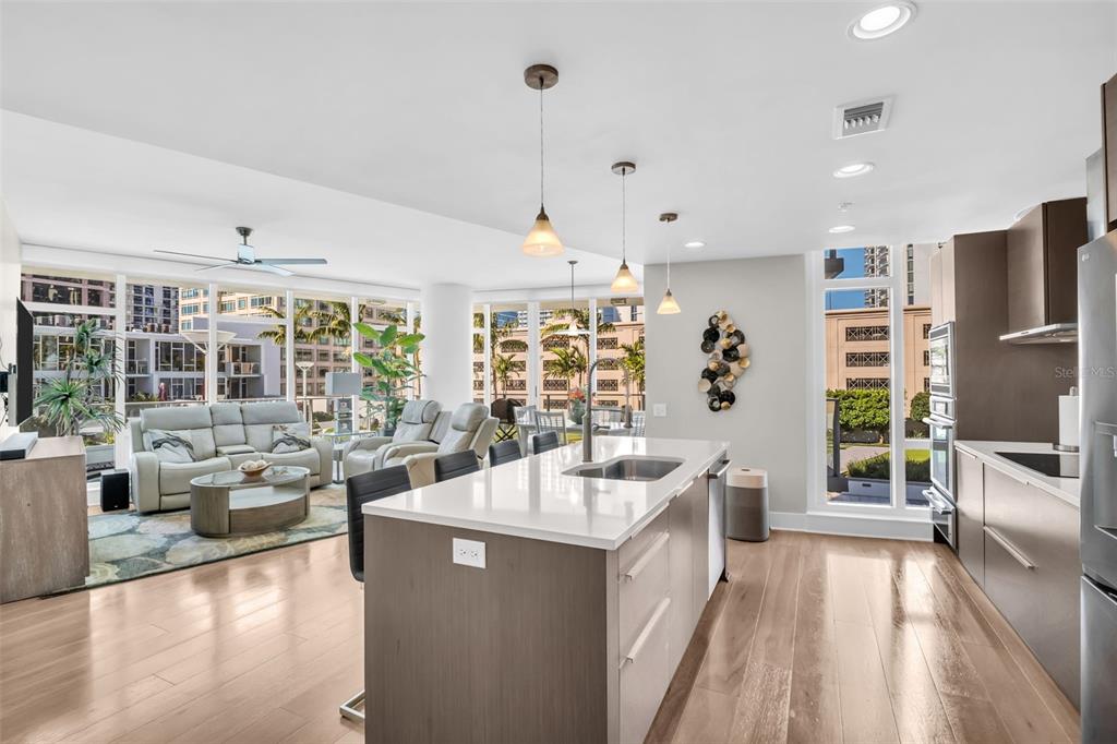 A modern open-concept kitchen and living area with hardwood floors, a kitchen island, and floor-to-ceiling windows — 175 1ST STREET S UNIT 702, ST PETERSBURG, FL