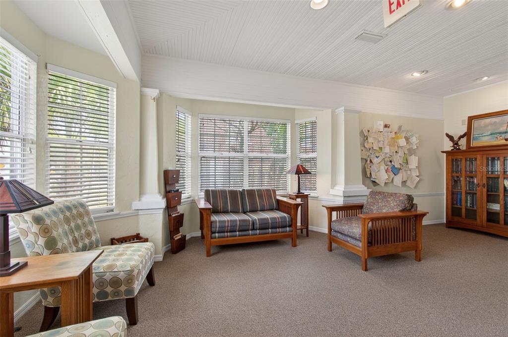 A sunlit sitting room features carpeted floors, wooden furniture, and a wall display of papers — 1013 SW 2ND AVENUE, GAINESVILLE, FL