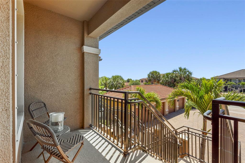 A covered balcony features two woven chairs and a metal railing overlooking a paved courtyard — 5420 CICERNONE STREET UNIT 203, SARASOTA, FL