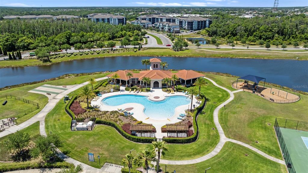 An aerial view shows a community swimming pool, clubhouse, playground, and tennis court by water — 16673 WINDMILL FORGE PASS, WIMAUMA, FL