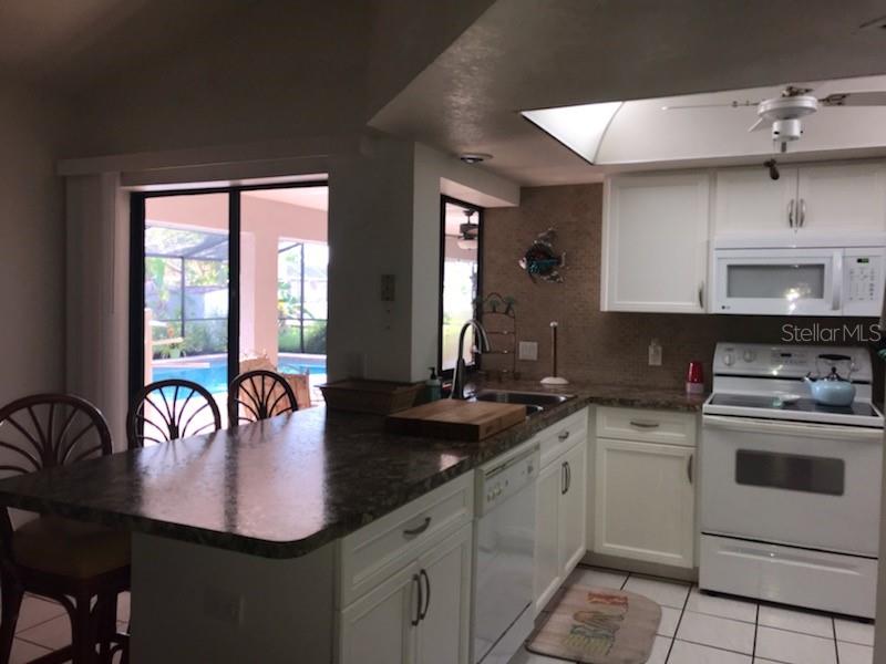 A kitchen with white cabinets, dark countertops, and a view of a pool through sliding doors — 7160 CARLSBAD TERRACE, ENGLEWOOD, FL