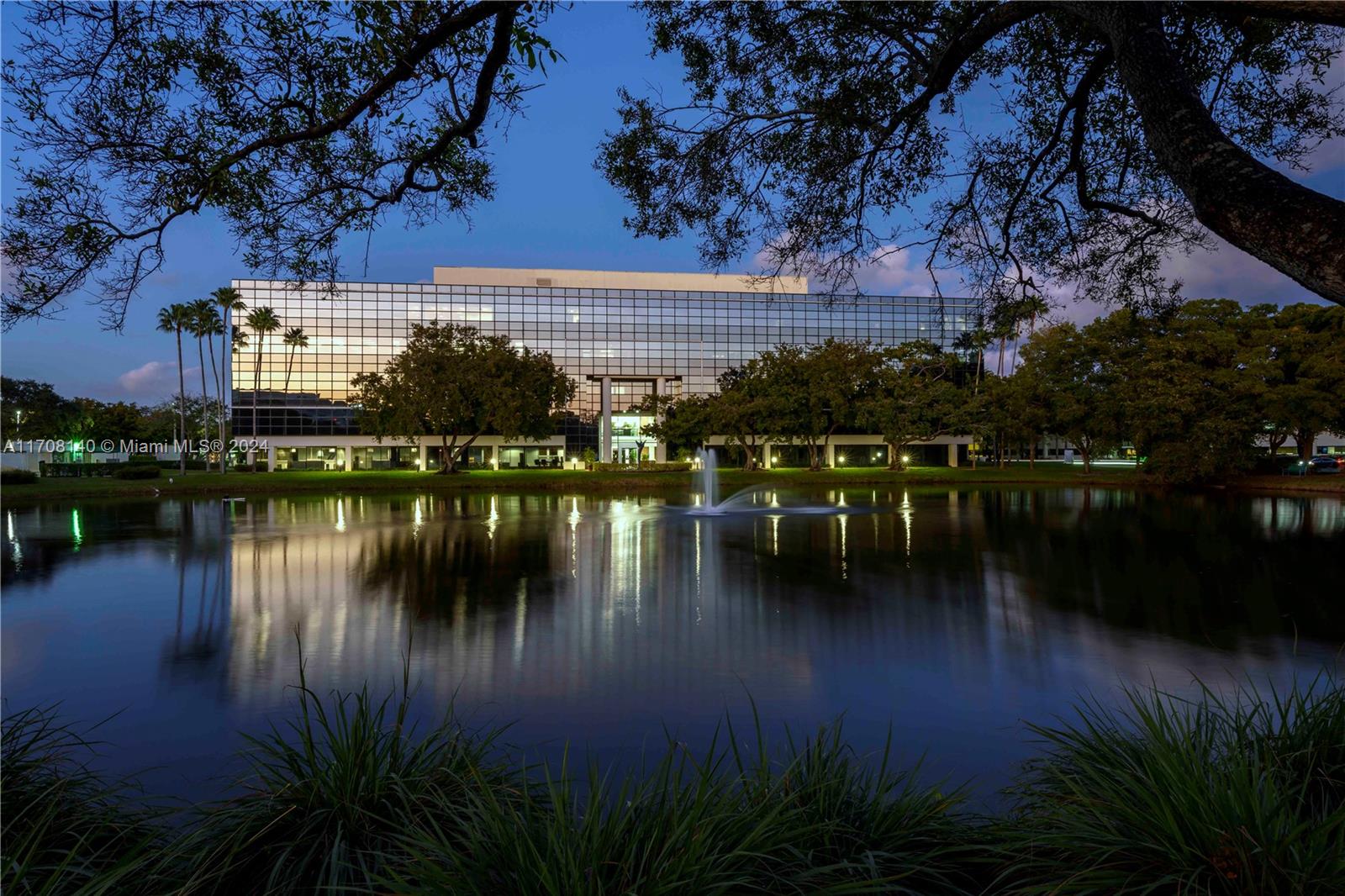 A modern office building stands behind a pond with a fountain at twilight — FORT LAUDERDALE, FL