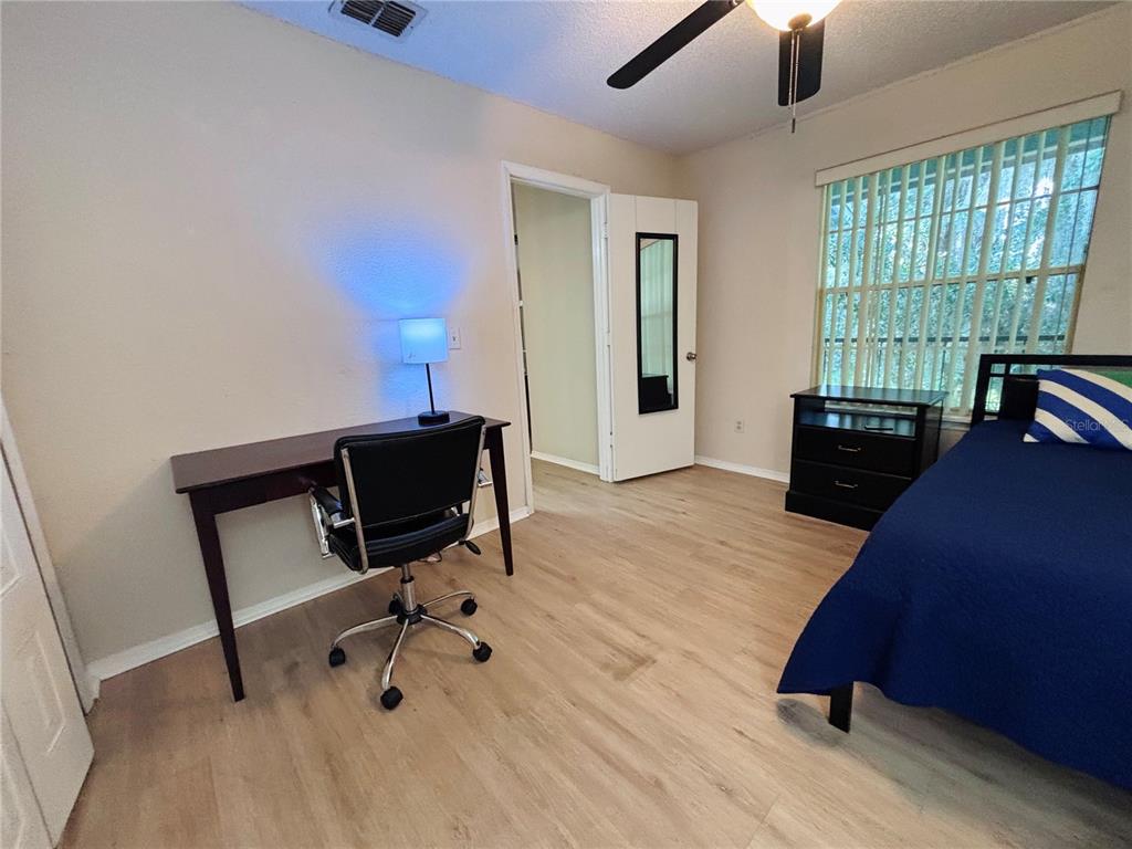 A bedroom features light wood-look flooring, a desk with a chair, and a bed — 2550 N ALAFAYA TRAIL UNIT 12203, ORLANDO, FL