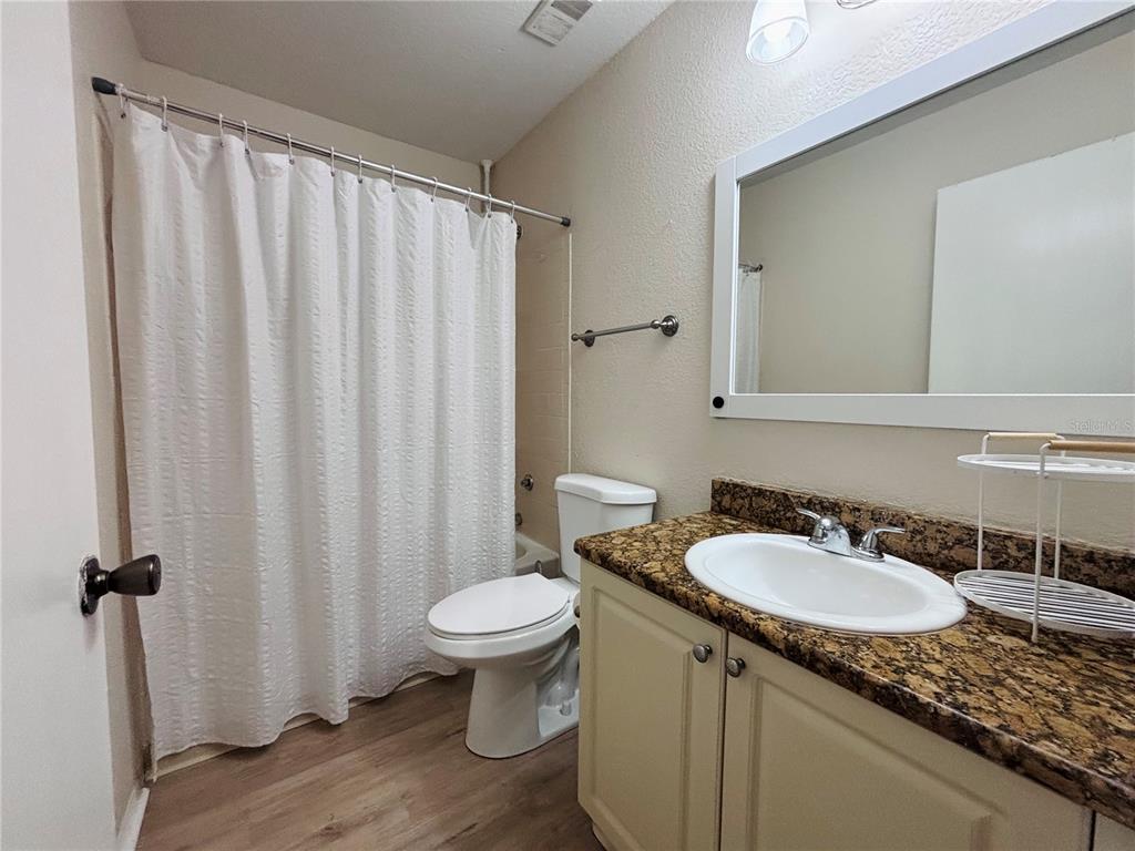 A bathroom features a white shower curtain, a toilet, and a vanity with a granite countertop — 2550 N ALAFAYA TRAIL UNIT 12203, ORLANDO, FL