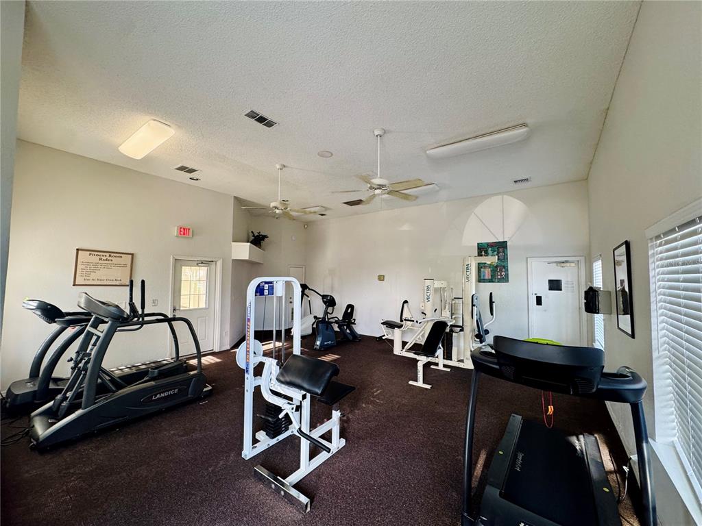 A fitness room features several exercise machines, ceiling fans, and carpeted flooring — 2550 N ALAFAYA TRAIL UNIT 12203, ORLANDO, FL